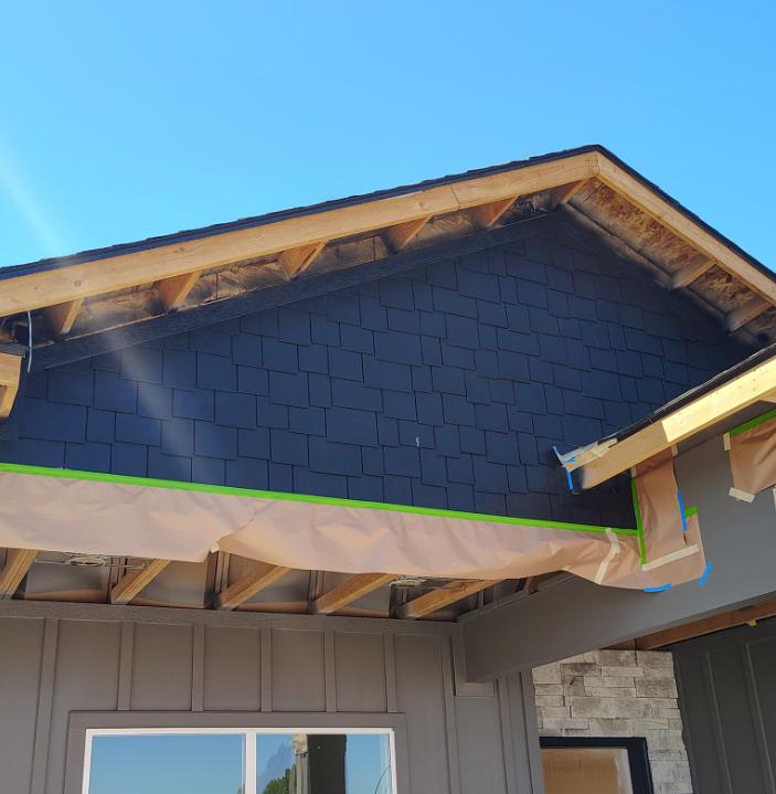 Exterior shingle siding being painted dark navy blue with masking tape in Twin Falls Idaho